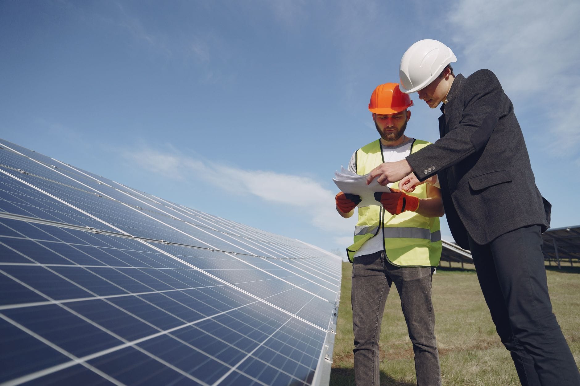 Elektryk i inspektor w kaskach analizują dokumenty przy panelach fotowoltaicznyc