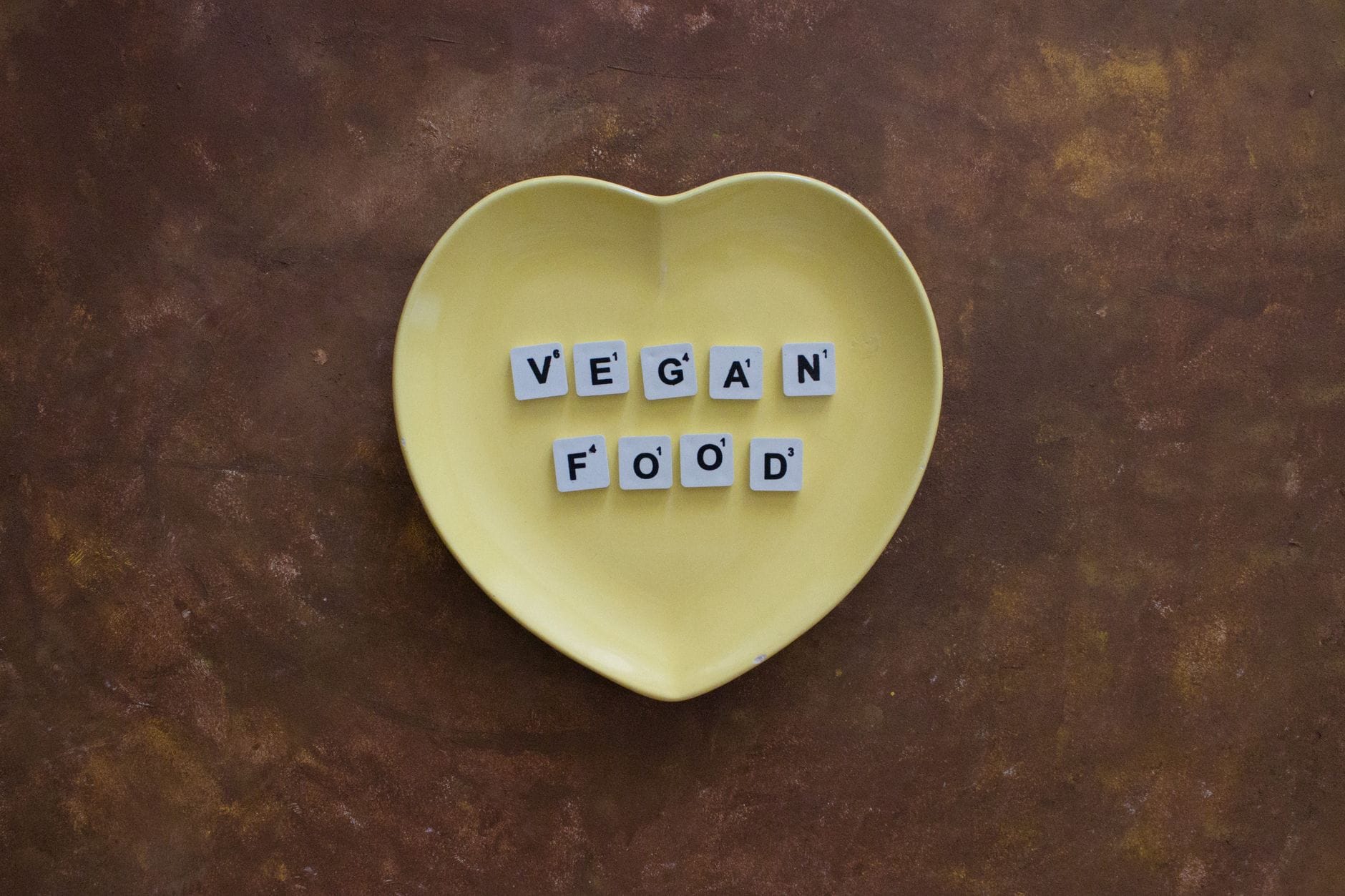 Żółty talerz w kształcie serca z napisem vegan food na drewnianym tle