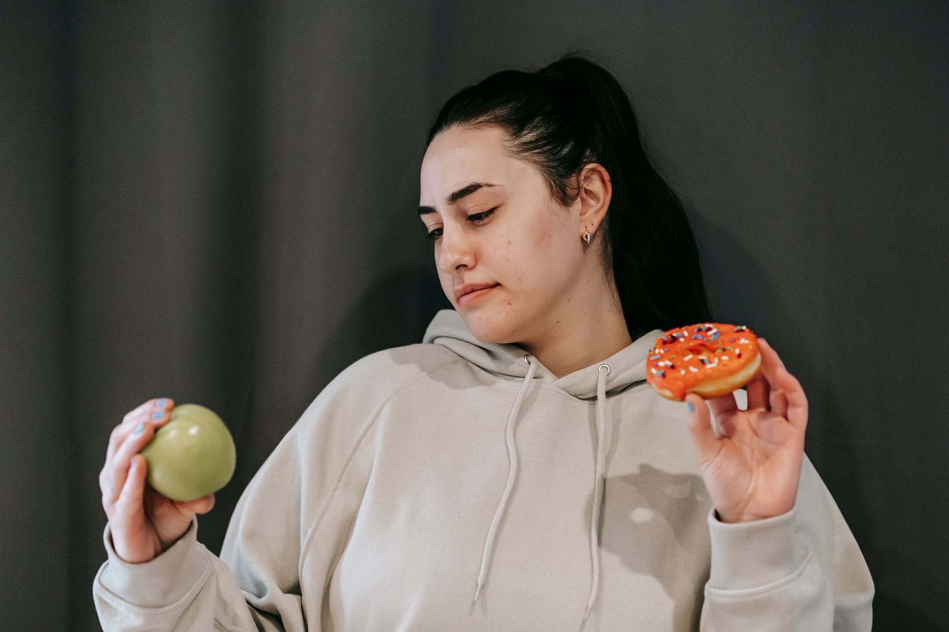 Kobieta w bluzie rozważa wybór między jabłkiem a donutem